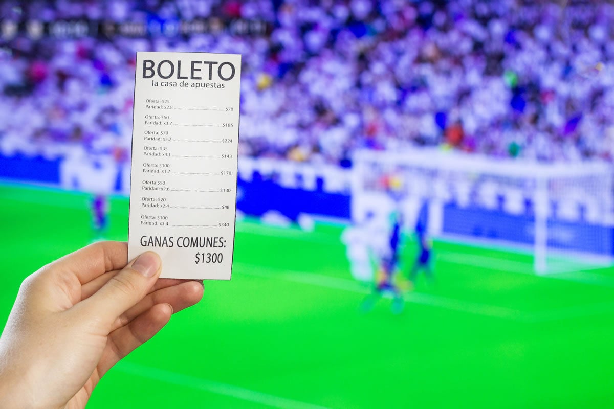 A woman's hand holds a bookmaker's ticket against the backdrop of a game of football.