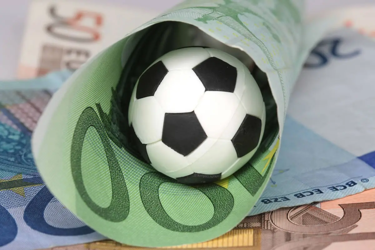 A football lies in a rolled-up 100 euro note.